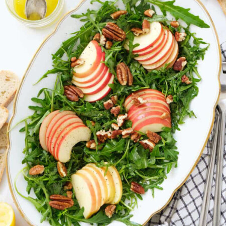 Top view of a white serving plate full of arugula apple salad.