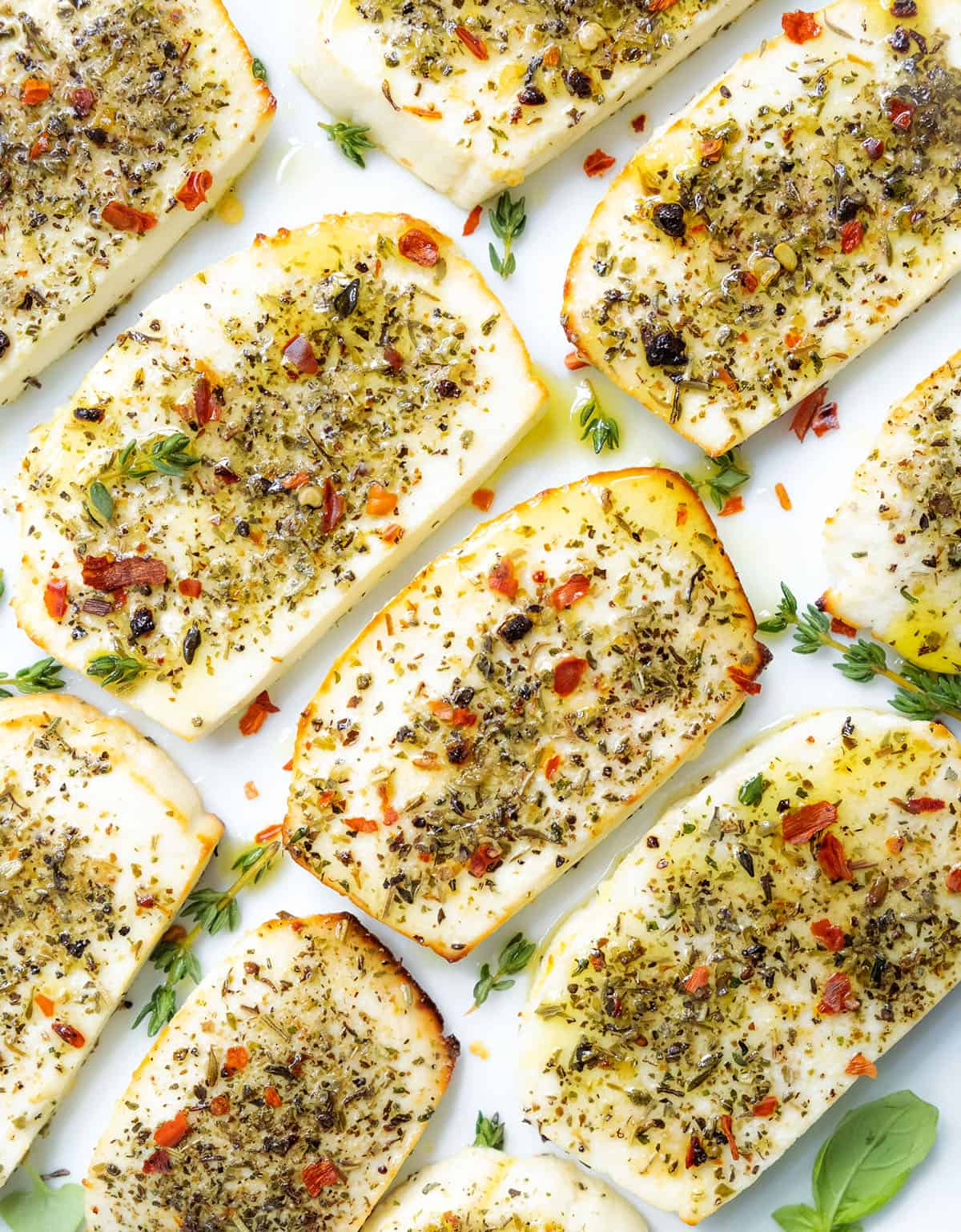 Top view of slices of baked ricotta sprinkled with herbs and served on a white plate.