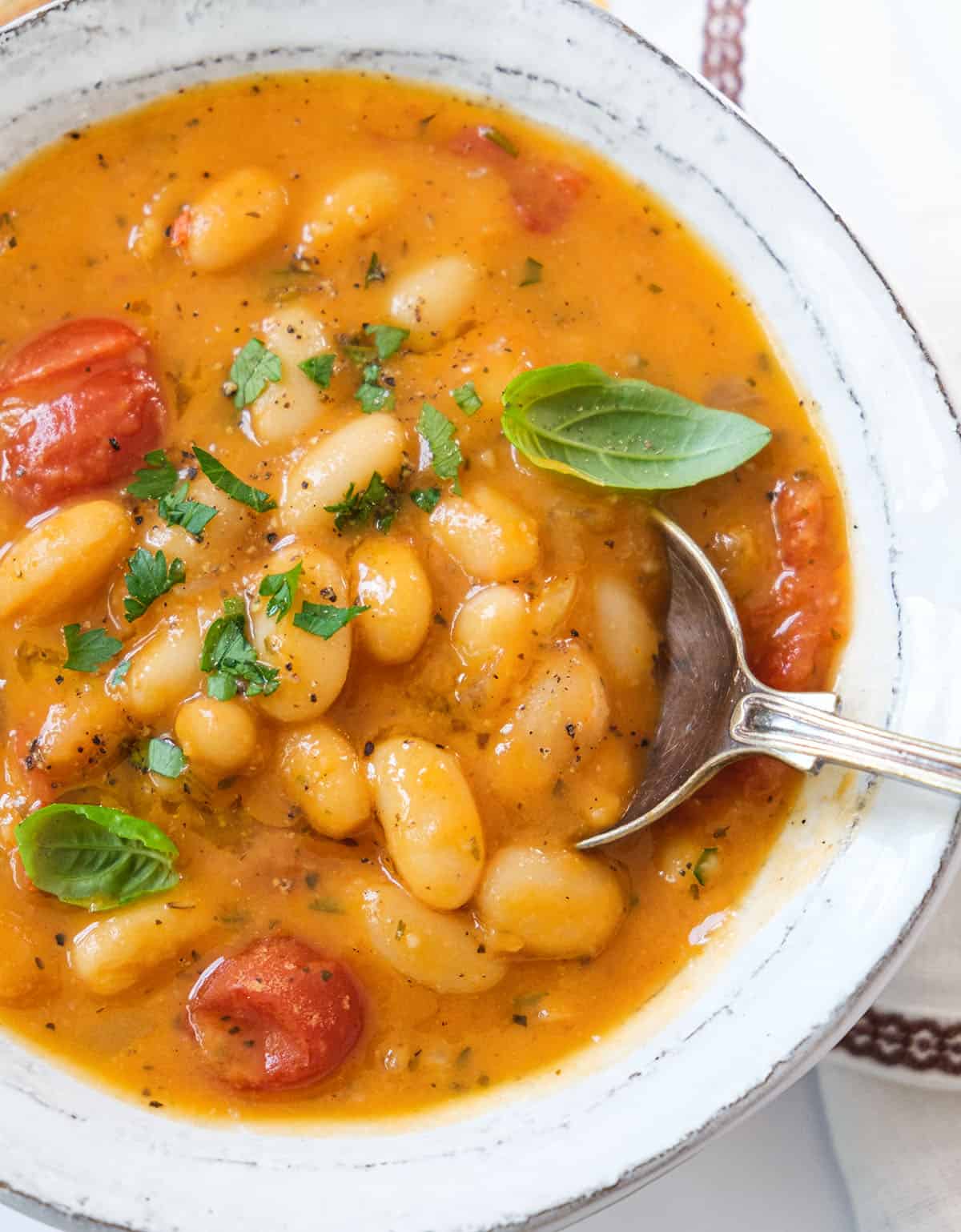 Top view of a white bowl full of creamy white bean soup garnished with fresh basil leaves.