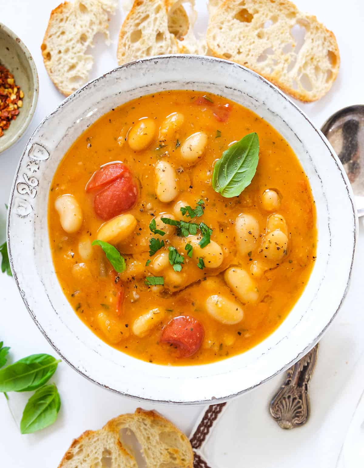 Top view of a white bowl full of cannellini bean soup served with crusty bread.