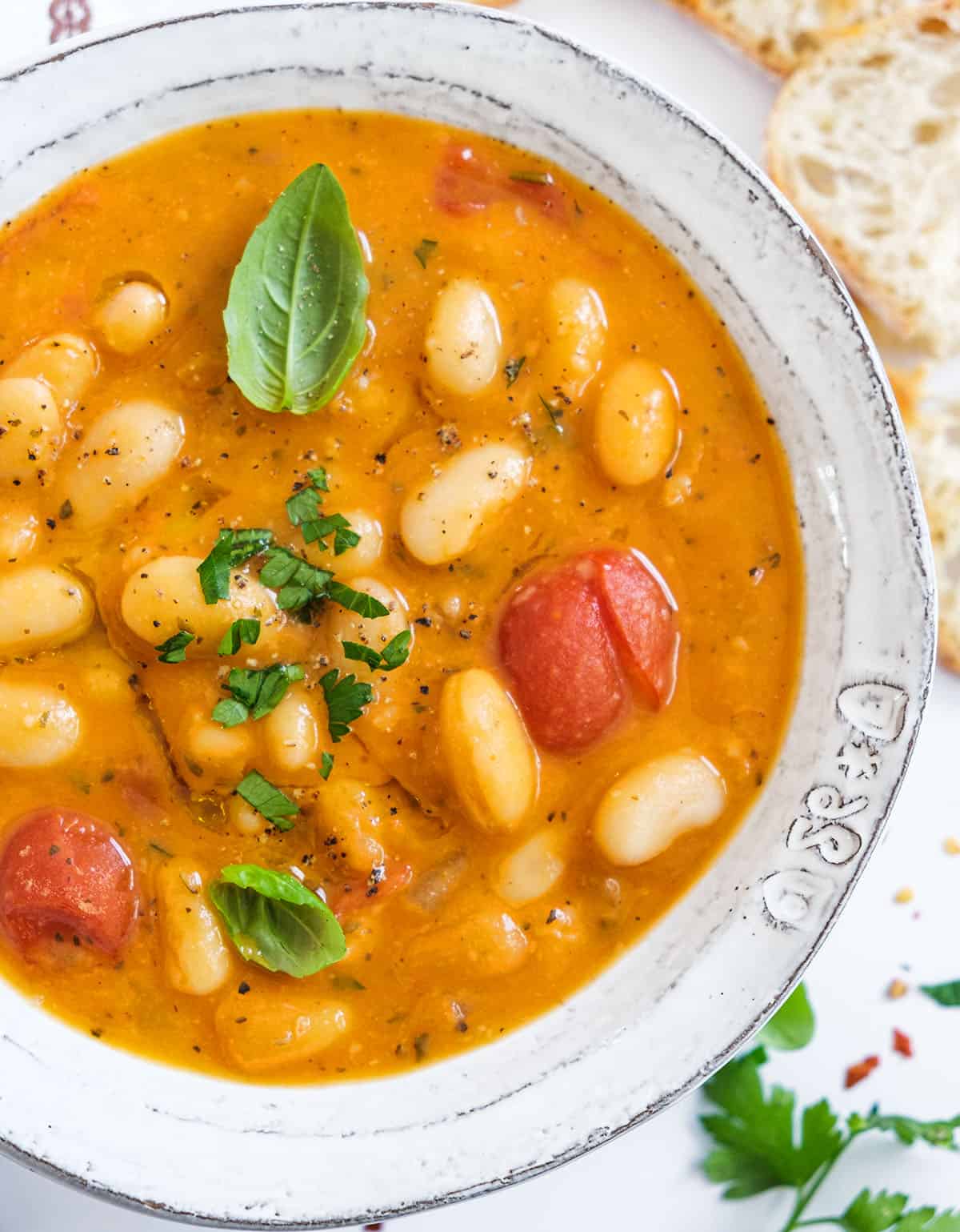 Top view of a white bowl full of white bean soup garnished with fresh herbs.