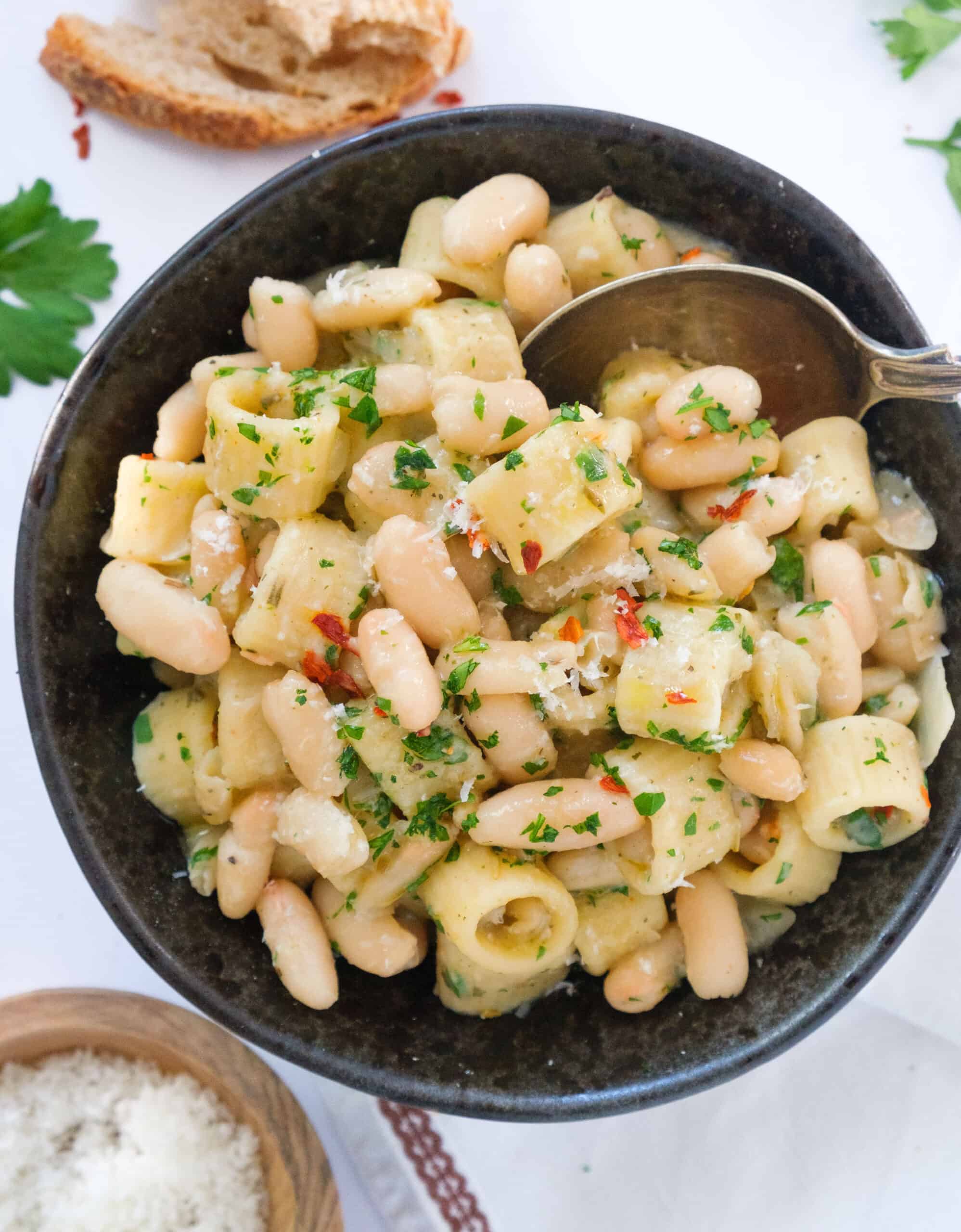 Top view of a dark bowl full of pasta with cannellini beans.