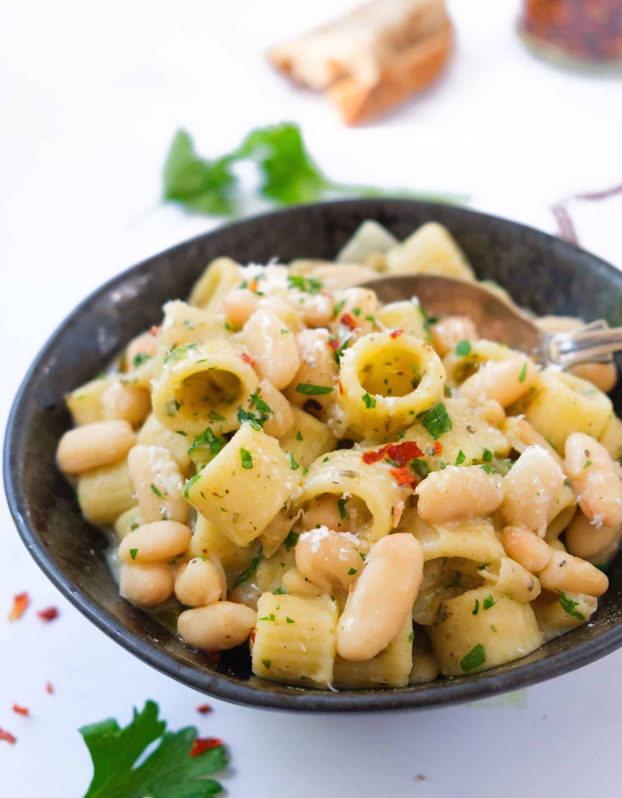 Close-up of a black bowl full of pasta with cannellini beans.