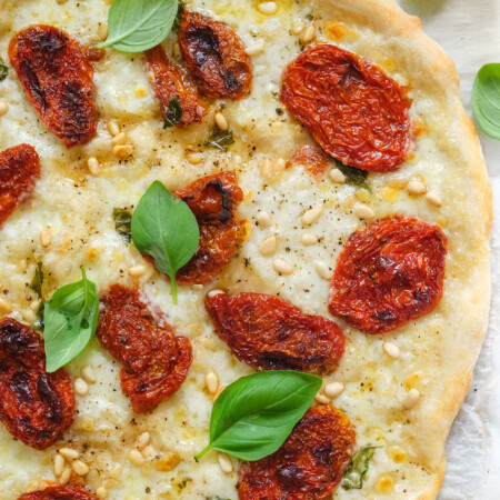 Top view of a sun-dried tomato pizza with fresh basil leaves.