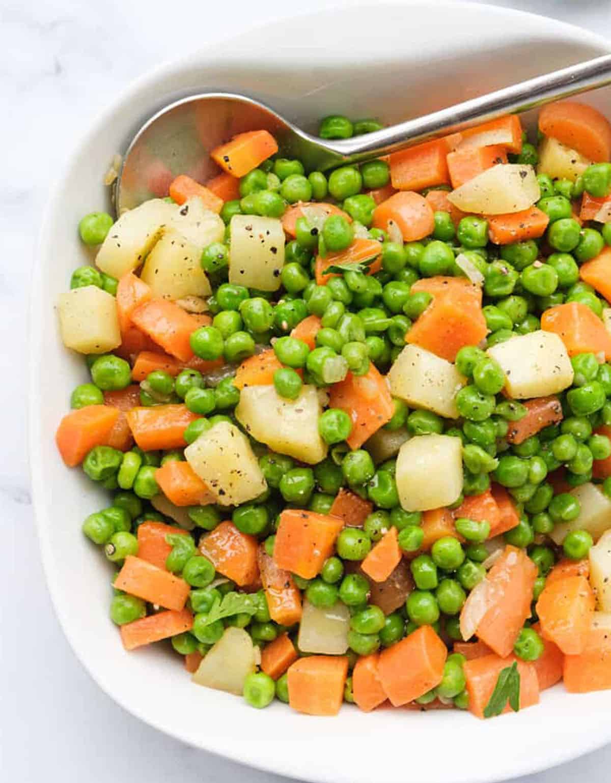 Top view of a square white serving plate with peas and carrots with cubed potatoes.