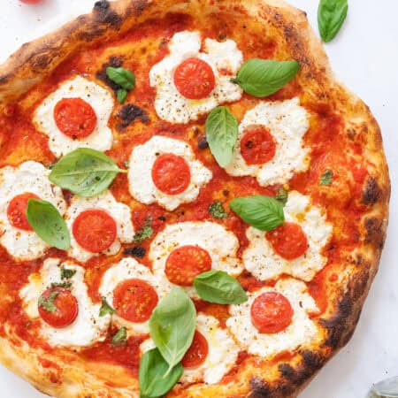 Top view of a ricotta pizza with cherry tomatoes and basil.