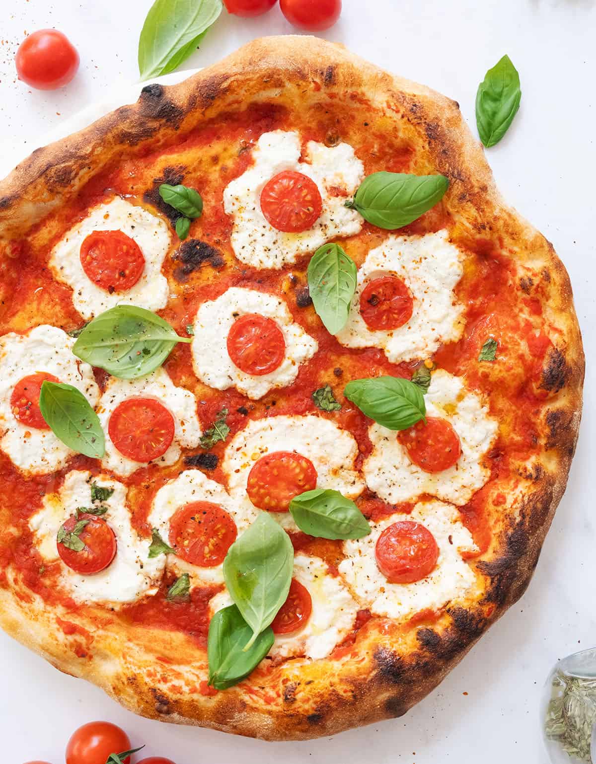 Top view of a ricotta pizza with cherry tomatoes and fresh basil.