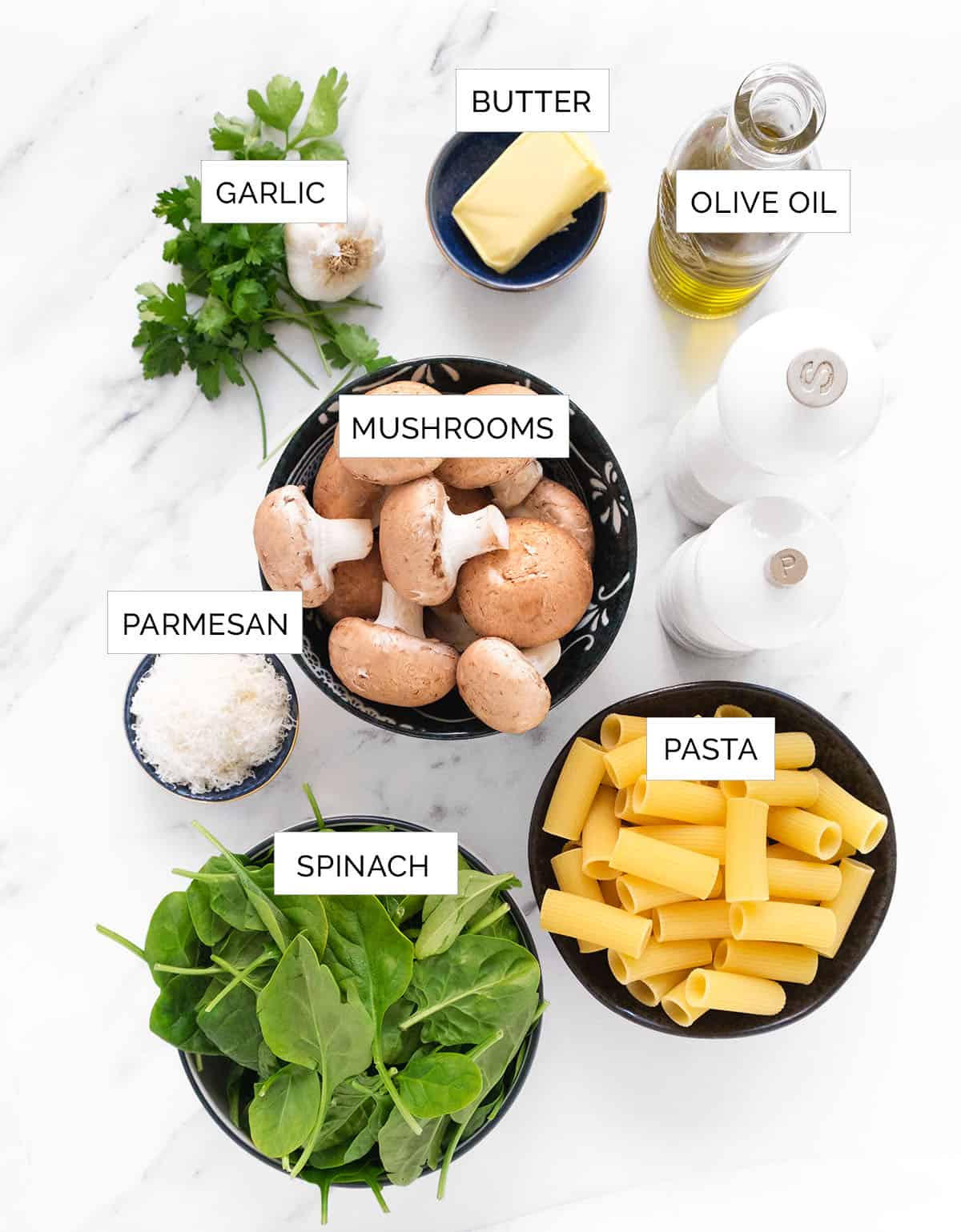 The ingredients to make spinach mushroom pasta are arranged over a white background.