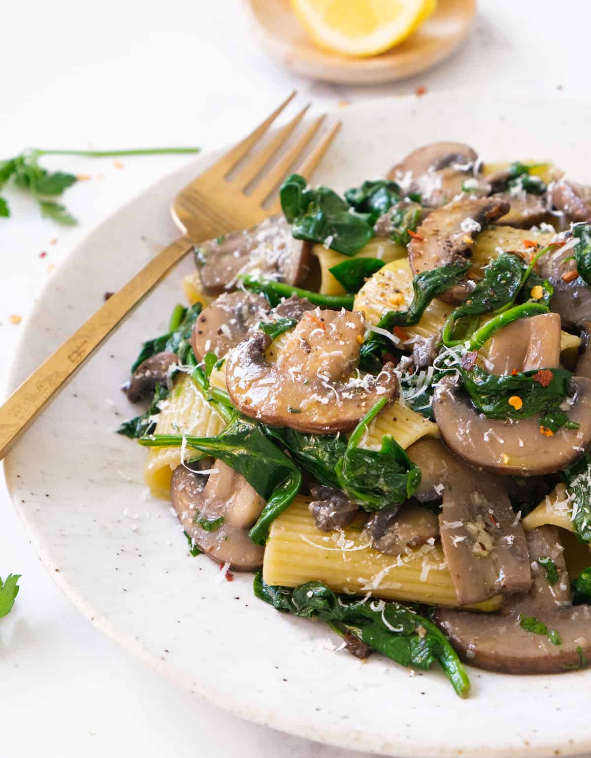 Close-up of a white plate full of spinach mushroom pasta.