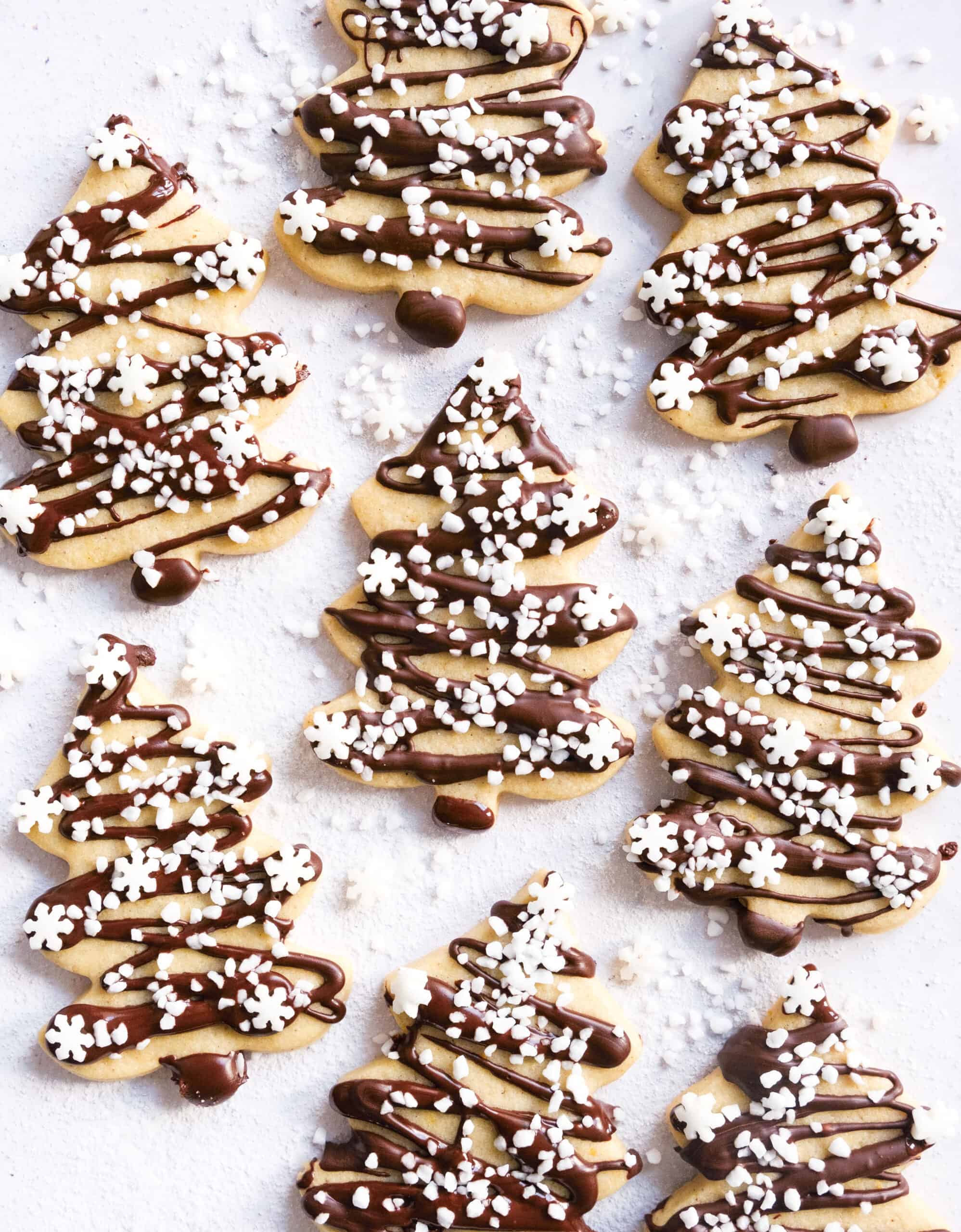 Top view of some Christmas tree cookies decorated with dark chocolate and white sugar sprinkles.