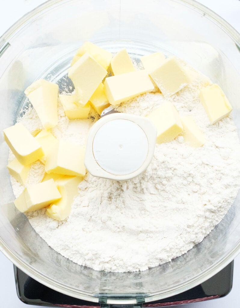 Top view of a food processor containing flour and butter.