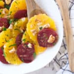 Beetroot orange salad with walnuts over a white serving plate.
