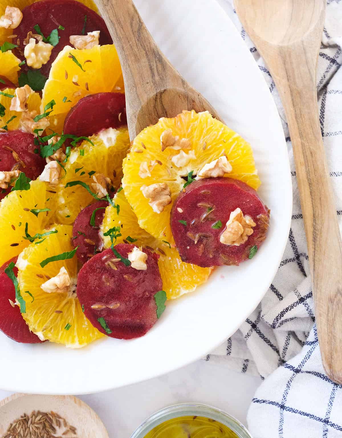 Top view of a white plate full of beetroot orange salad garnished with parsley and walnuts.