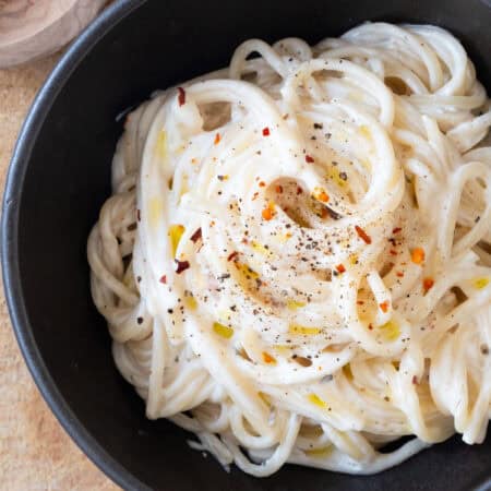 Close-up of a black bowl full of creamy spaghetti.