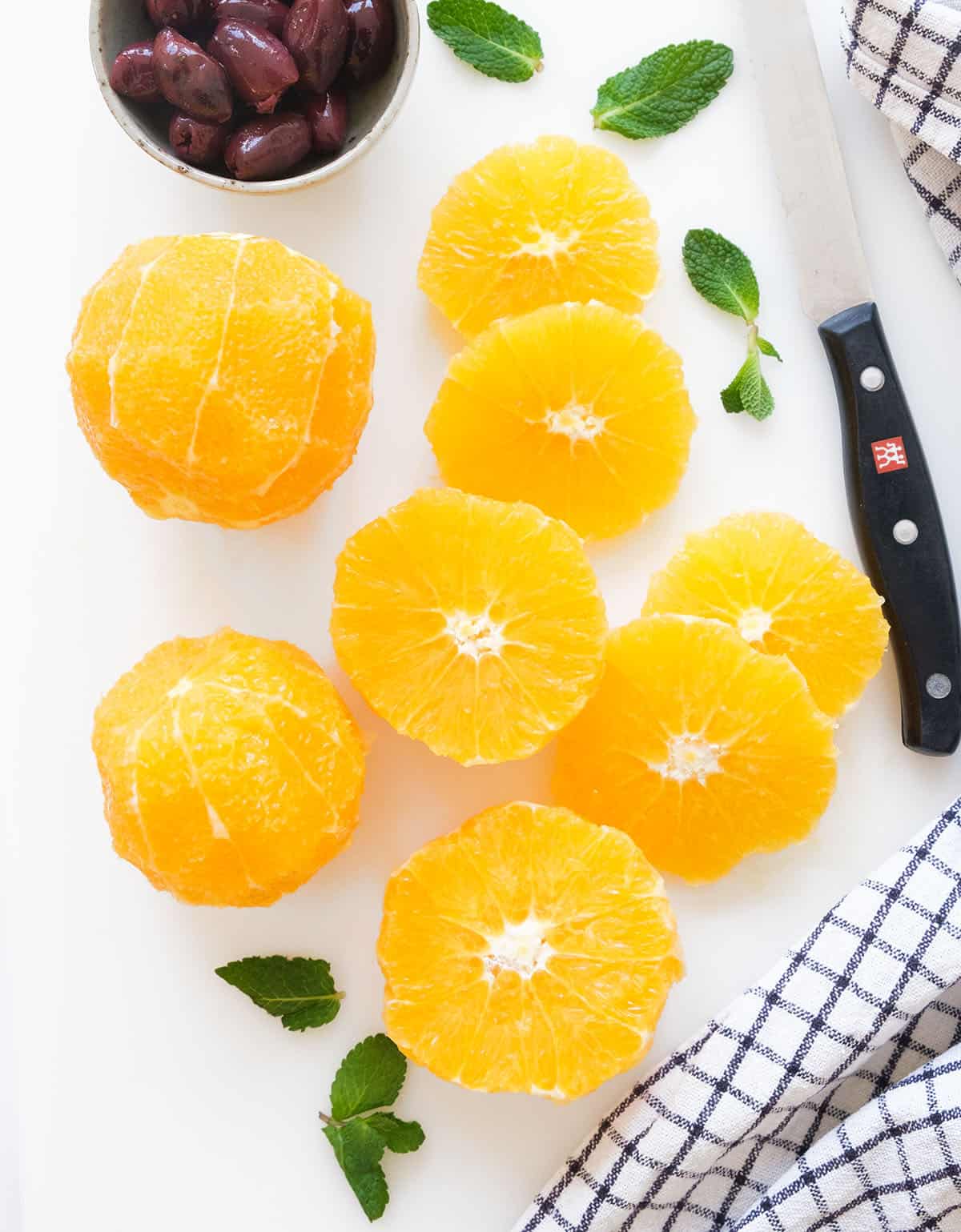 Top view of a knife and oranges sliced into rounds over a white background.