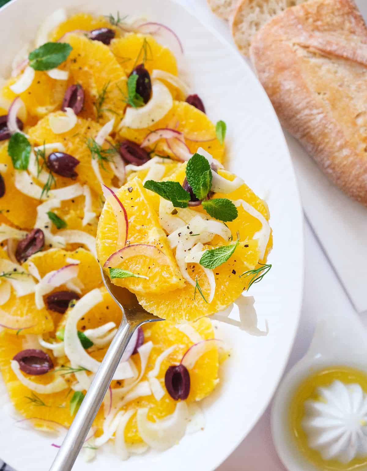 Top view of a white serving plate full of orange salad with mint leaves, olives and fennel.