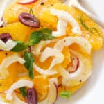 Top view of some orange salad with black olives on a white plate.