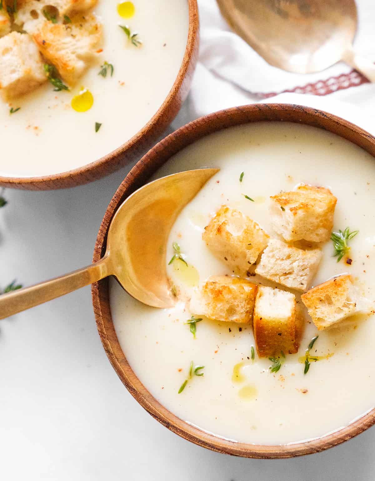 Close-up of a spoon and a bowl full of vegan cauliflower soup garnished with thyme and croutons.
