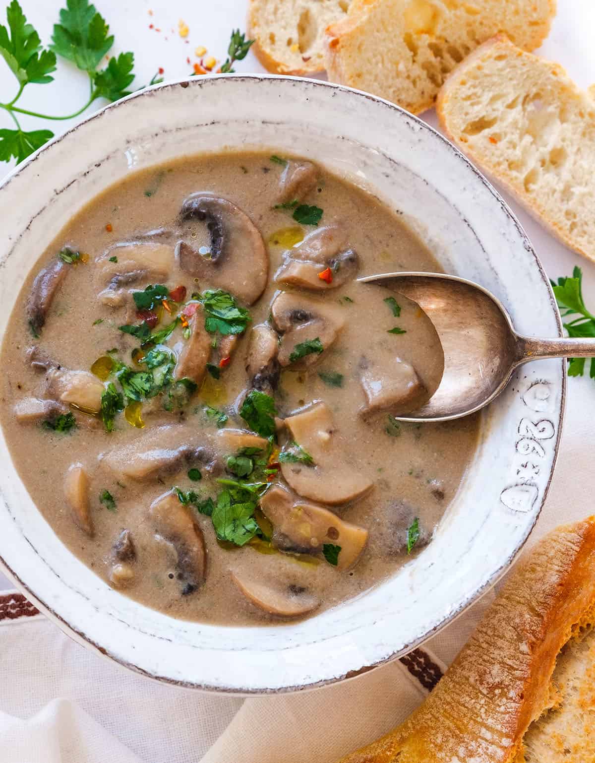 Top view of a white bowl full of creamy vegan mushroom soup served with crusty bread.