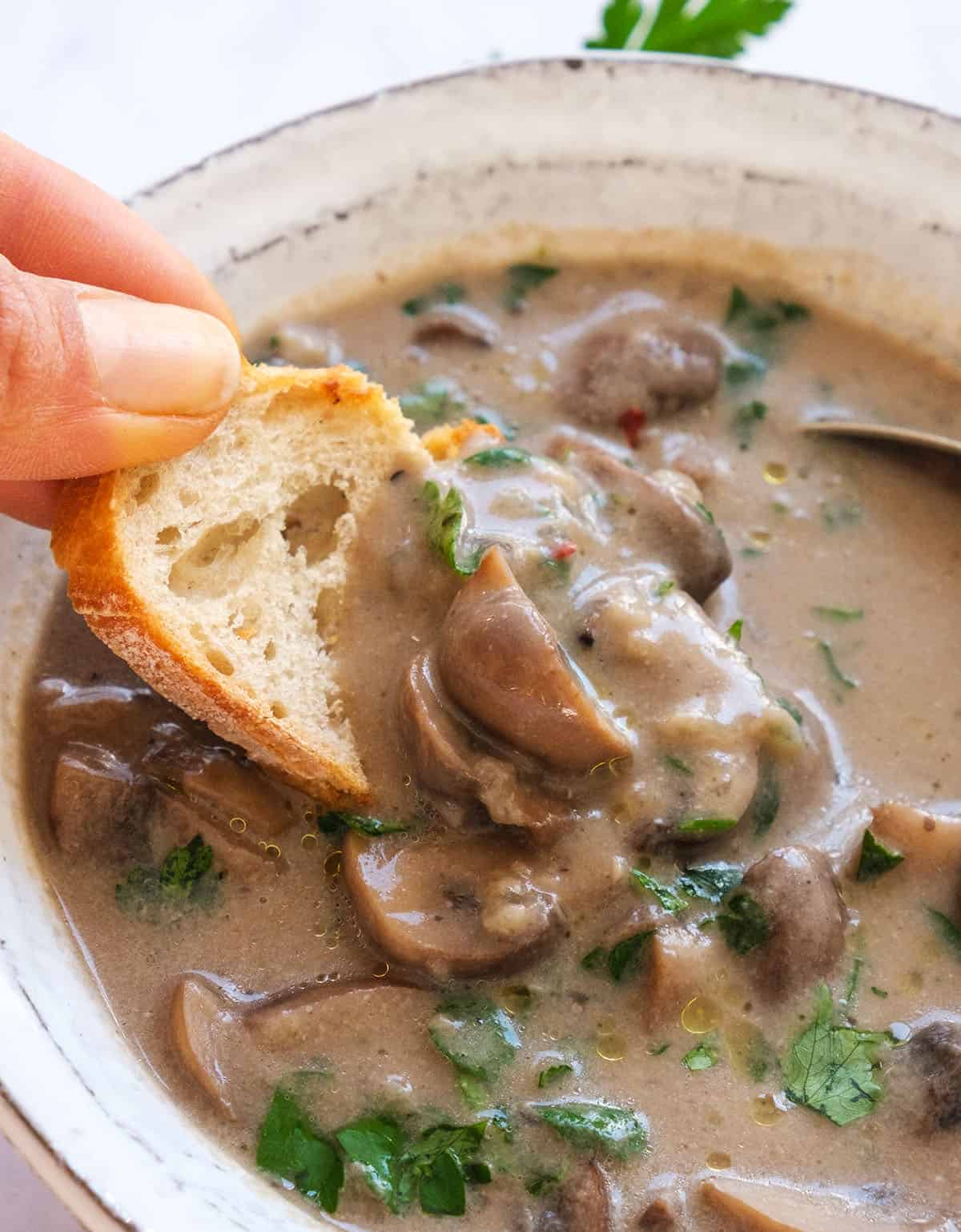 Close-up of a slice of bread dunking in the creamy vegan mushroom soup.