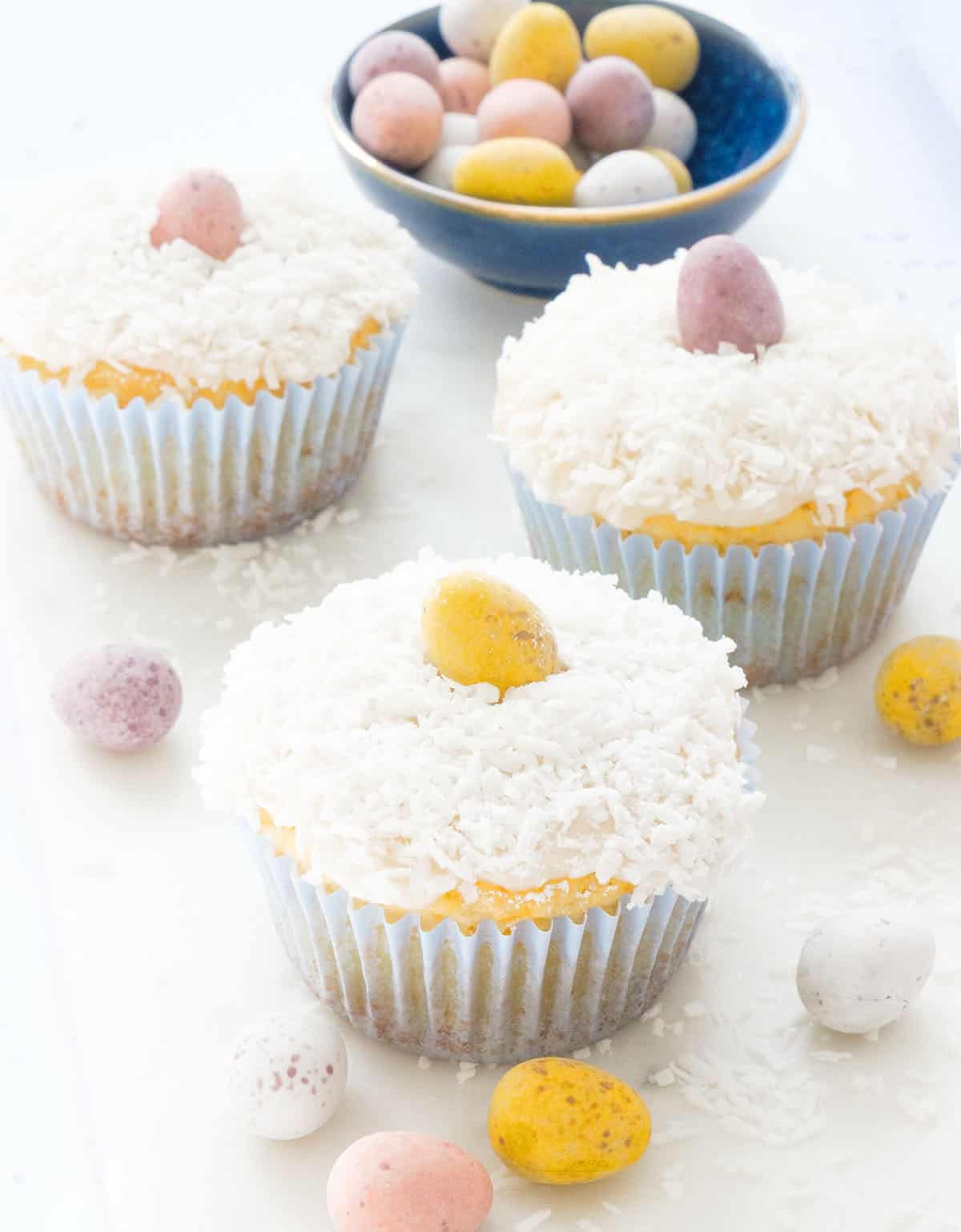 A few Easter muffins topped with coconut and mini chocolate eggs over a white background.