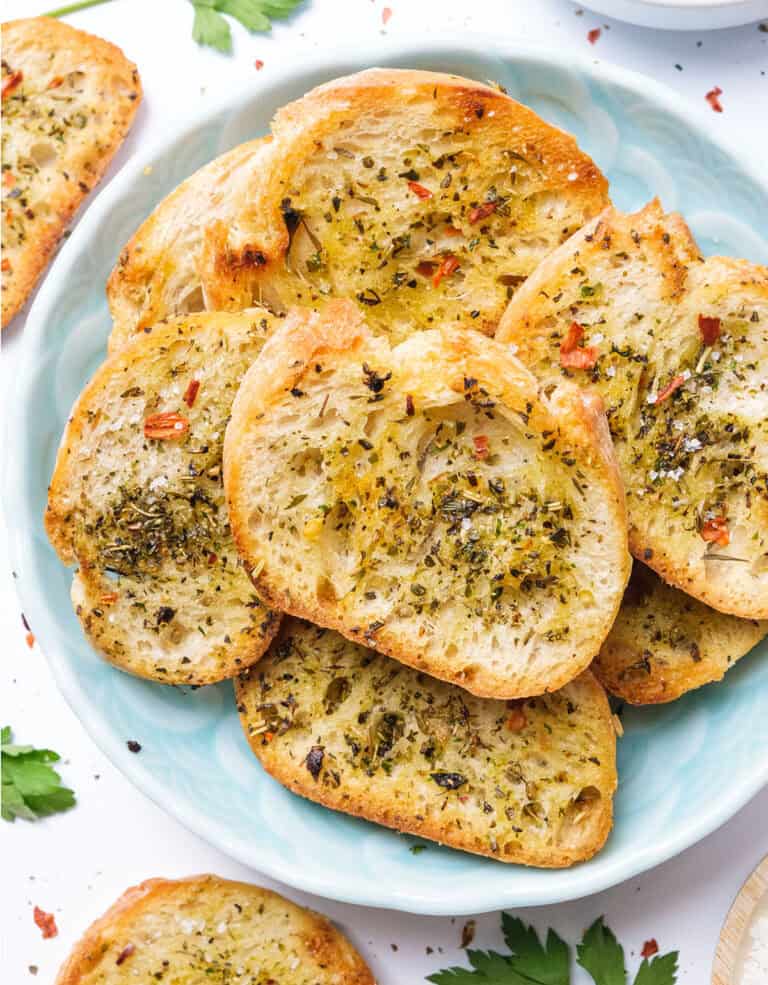 Top view of golden herbed Italian crostini on a light blue plate.