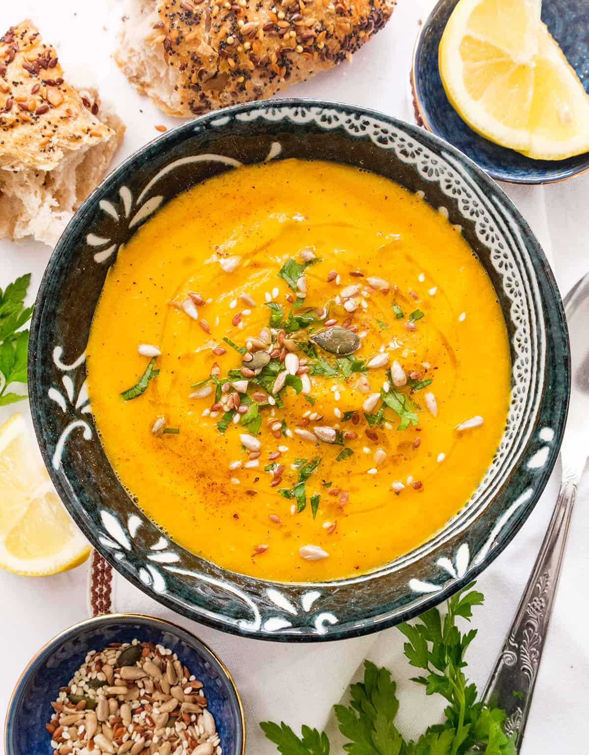 Top view of a black bowl full of creamy carrot and celery soup garnished with seeds.