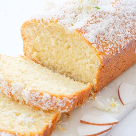 A coconut bread topped with grated coconut over a white background.