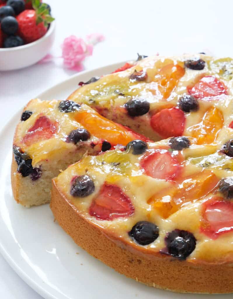 Close-up of glossy, juicy fruit cake topped with berries, kiwis and apricots.