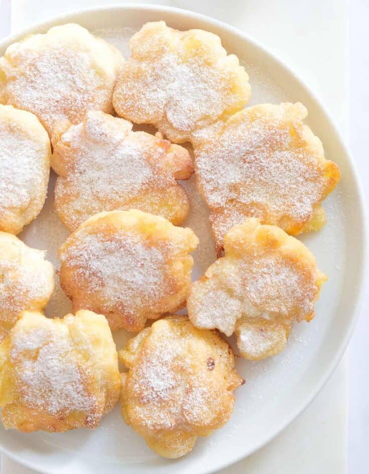 Top view of a white plate full of round apple fritters.