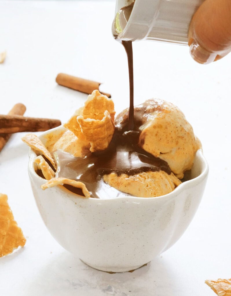 Melted dark chocolate is poured over a serving of pumpkin ice cream.