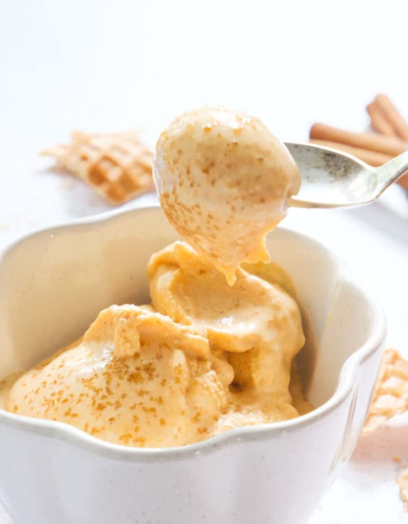 A spoon full of pumpkin ice cream over a white background.