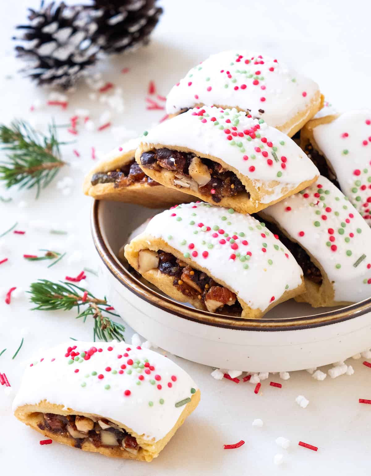Italian fig cookies topped with icing and sprinkles served in a white bowl.