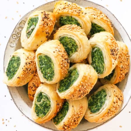 Top view of spinach puff pastry bites served in a white bowl over a white background.