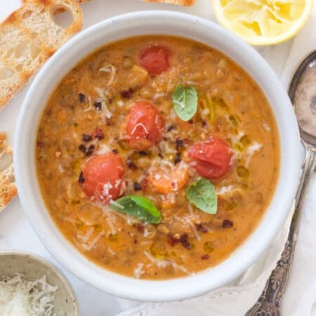 Top view of a white bowl full of creamy lentil soup with tomatoes and basil leaves.