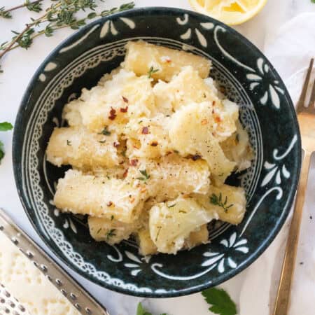 Top view of a dark bowl full of pasta with cauliflower.