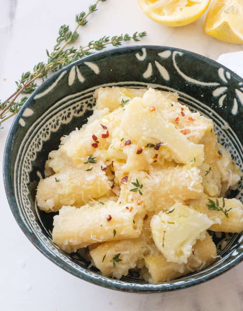 Close-up of a dark bowl full of pasta with cauliflower.