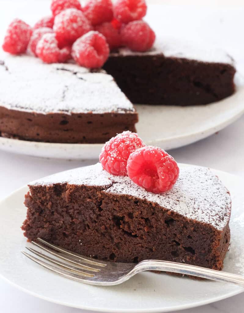 A chocolate ricotta cake topped with raspberries over a white background.