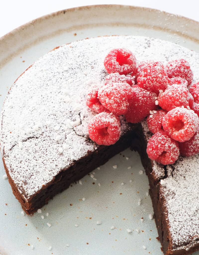 Close-up of a chocolare ricotta cake topped with raspberries and powedered sugar.