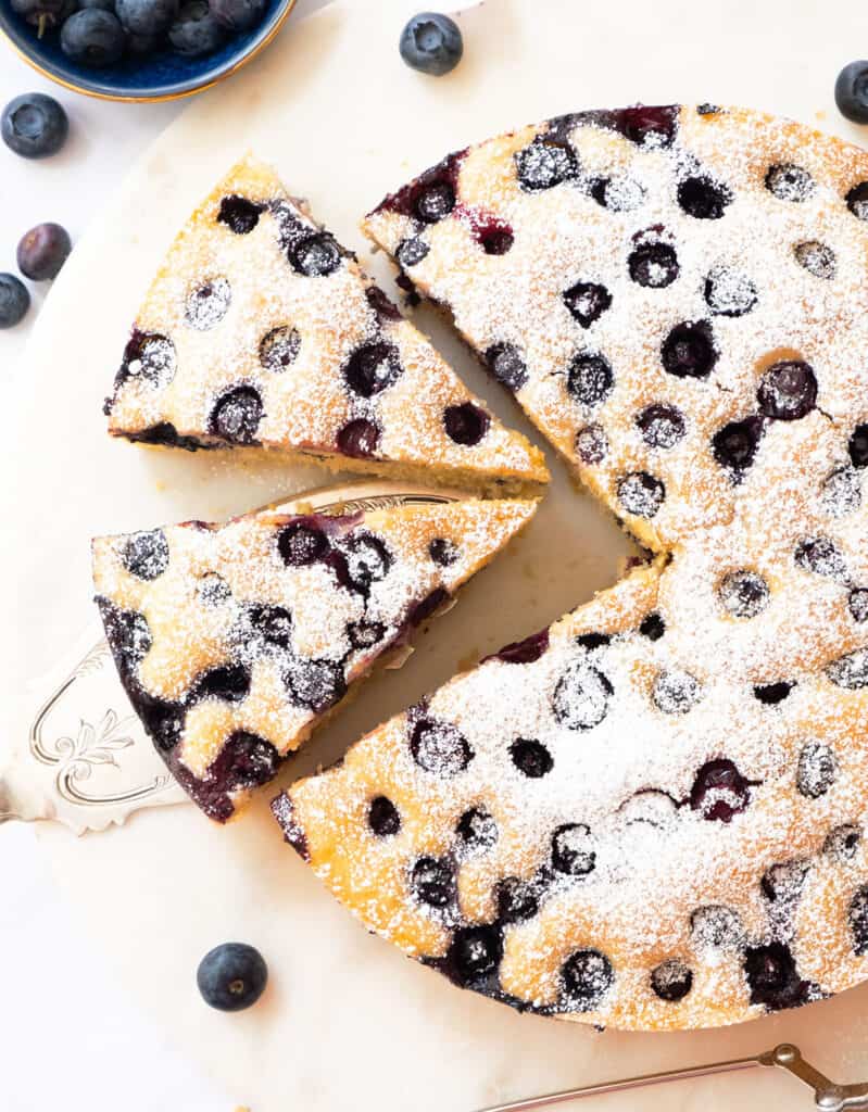 Top view of a ricotta blueberry cake cut into slices and dusted with powdered sugar.