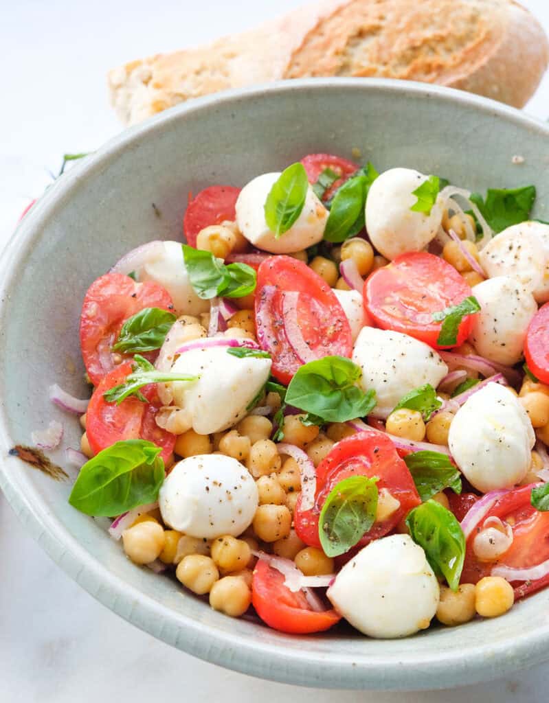 A bowl full of Italian chickpea salad with mozzarella and fresh basil.