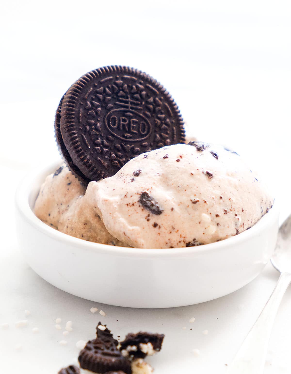 A total white background and white bowl with oreo ice cream topped with an oreo cookie.