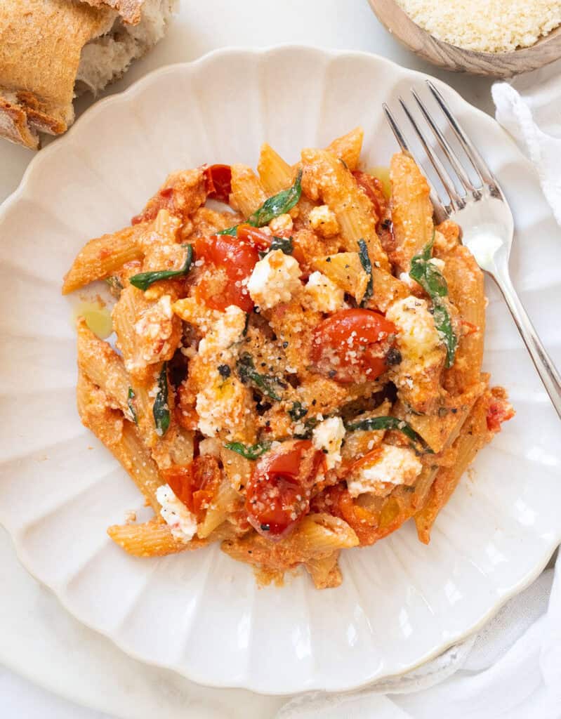 Tomato and ricotta pasta with basil on a white plate.
