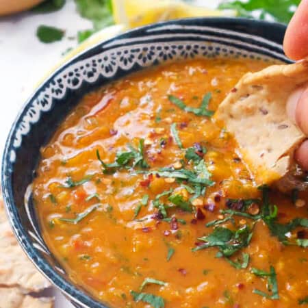 A blue bowl full of tomato lentil soup and chopped coriander.