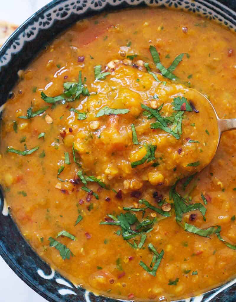Top view of bowl and a spoon full of thick, creamy tomato lentil soup and chopped cilantro leaves.