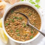 A white bowl full of green lentil soup served with bread.