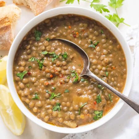 A white bowl full of green lentil soup served with bread.