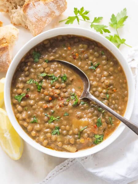 A white bowl full of green lentil soup served with bread.