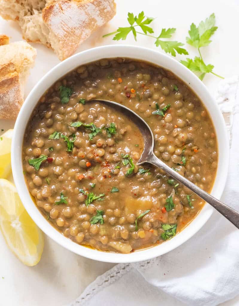 A white bowl full of green lentil soup served with bread.