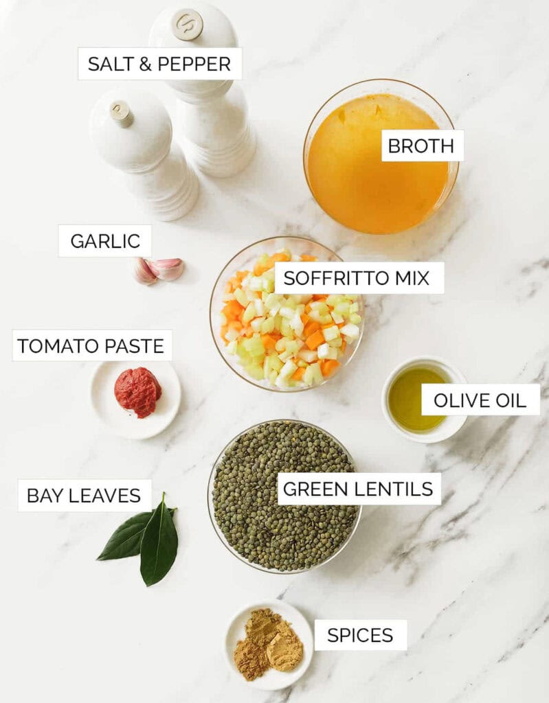 The ingredients for this green lentil soup are arranged over a white marble table.